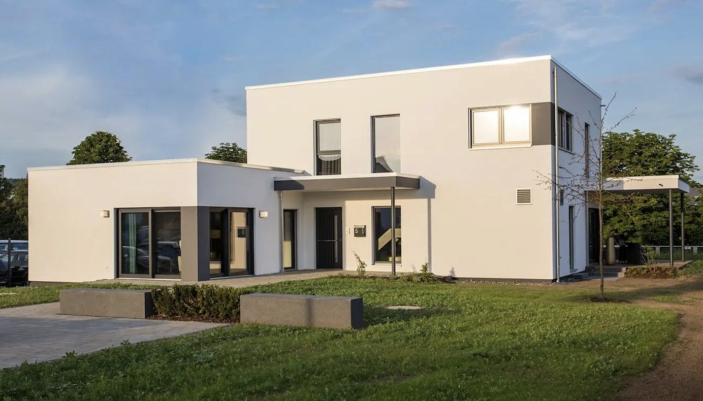 Modernes weißes Haus mit Flachdach, großen Fenstern und Rasen